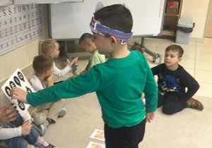 chłopiec pokazuje odpowiednią literkę- zabawa w poznawanie samogłosek