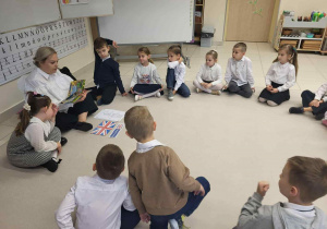 Dzieci siedzą w kole wraz z Pania, które opowiada i pokazuje na obrazkach symble Wielkiej Brytanii