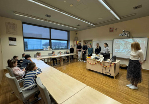 dzieci siedzą w ławkach patrząć i słuchając powitania w języku niemieckim