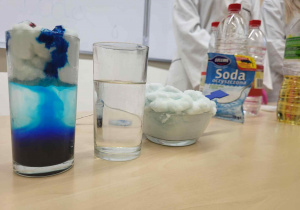 trzy szklanki stojące na stole, w których pokazane są różne doświadczenia chemiczne