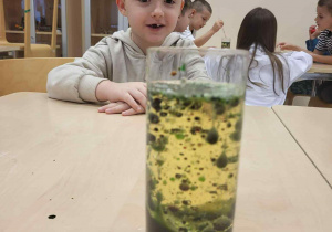 chłopiec siedzie przy stoliku i obserwuje so się dzieje w szklance z wodą po dolaniu oleju