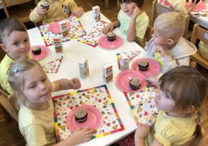 dzieci siedza przy stole i jedza babeczki