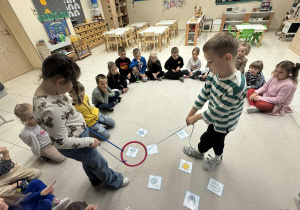 chłpiec i dziewczynka trzymają w rękach sznurki przymocowne do koła i muszą według polecenia znalezć odpowiedni obrazek z pogodą