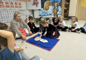 dzieci za pomocą maty edukacyjnej układają części ciałą i ubrań misia
