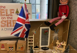 Elf psotnik siedzi przy oknie na swoim domku z kartonu