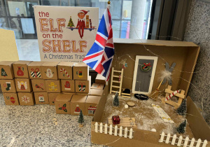 na parapecie przy oknie znajduję się domek elfa psotnika, ponumerowane pudełeczka kalendarza adwentowego i książka anglojęczyna "Elf on the shelf"