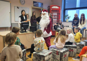 dzieci siedzą w kręgu i witają się w języku angielskim z mikołajem a za nim stoi Pani od angielskiego i uczniowe