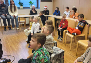 dzieci siedzą w kręgu a za nimi w ławkach uczniowe liceum