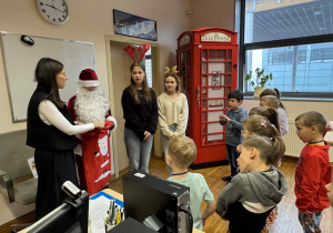 dzieci stoją przed mikołajem i Panią od angielskiego, słuchając polecenia do zadania