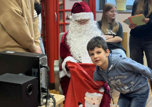 chłopiec sięga do worka z prezentami, który trzyma mikołaj