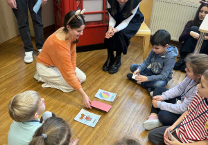 dzieci siedzą w kole wraz z uczenicą i Panią od angielskiego, bawią sie w zabawe "what's missing"?