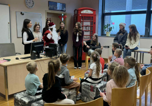 dzieci siedzą w kręgu i słuchaja co mówi do nich mikołaj, obok,którego jest Pani od angielskiego i uczniowie