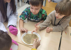 chłopcy siedzą przy stoliku z uczenicą liceum i obserwują doświadczenie z pieprzem