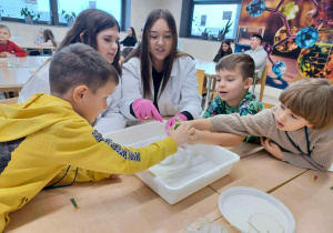 dzieci siedzą przy stoliku z uczenicami i dotykają cieczy nienewtonowskie