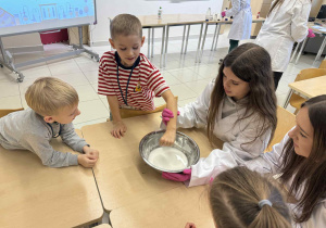 dzieci siedzą przy stoliku z uczenicami i dotykają cieczy nienewtonowskiej