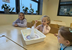 dziewczynki siedzą przy stoliku i obserwują erupcje wulkanu