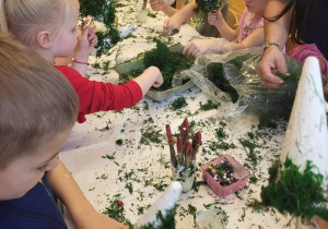 dzieci obklejają choinkę mchem