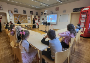 dzieci siedzą przy stolikach i oglądaja bajke w jęzku angielskim o reniferach mikołaja