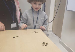 chłopiec i dziewczynka stoją przy stoliku i obserwują eksperyment z monetami