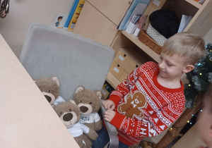 chłopiec stoi przy biurku i patrzy na misie, które siedzą na miejscu Pani