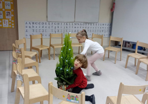 chłopiec i dziewczynka stoją w kole z ustawionych krzeseł i sprzątają rzeczy, które elf napsocił