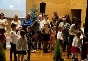 dzieci z rodzicami stoją na scenie i śpiewają kolędy