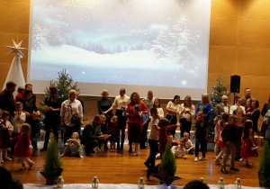 Rodzice, dzieci oraz nauczycielki śpiewają na scenie kolędy