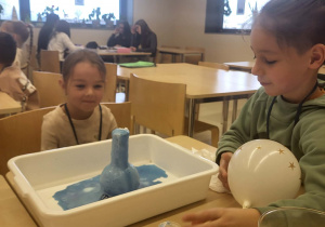 dziewczynka i chłopiec obserują doświadczenie chemiczne