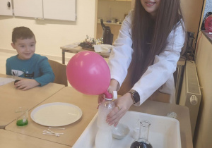 uczenica pokazuję doświadczenie z balonem,obok siedzi uśmiechniety chłopiec