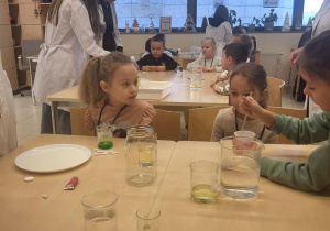 dziewczynki i chłopiec siedzą przy stoliku i wykonują doświadczenie