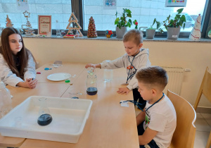 chłopcy i uczenica siedzą przy stoliku i wykonują doświadczenie chemiczne