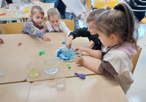 dziewczynki siedzą przy stoliku i wykonują doświadczenie chemiczne