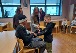 chłopiec ubiera ucznia w rękawiczki, obok nich stoją uczenice