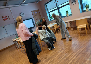 chłopiec ubiera ucznia w ubrania zimowe obok nich stoją uczenice