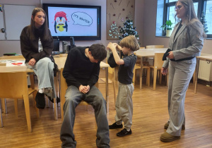 chłopiec ubiera ucznia w czapke, obok nich siedzi dziewczyna a druga stoi