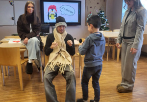 chłopiec ubiera ucznia w rękawiczki obok nich siedzi dziewczyna a druga stoi