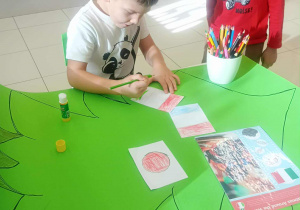 chłopiec siedzi i maluje flage a drugi obok niego stoi