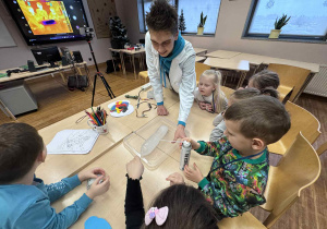 dzieci siedzą przy stoliku i jeden chłopiec trzyma ciecz w sprayu