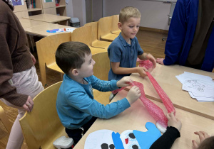 dwóch chłopców siedzi przy stoliku i trzymają folię bąbelkową