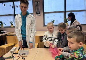 uczeń z liceum stoi uśmiechniety przy dziewczynkach i chłopcach trzymających folię bąbelkową