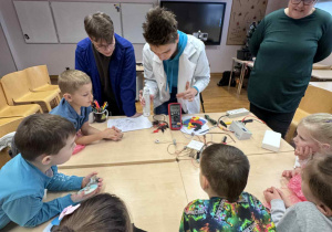 dzieci siedzą przy stoliku i obserwuja eksperyment,który wykonują uczniowe techniku i nauczycielka od fizyki