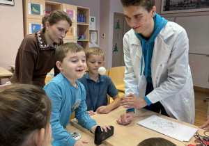 chłopiec z uśmiechnietą mina wykonuję eksperyment z latającą piłeczką z pomocą ucznia technikum