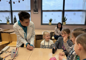 dziewczynka wykonuję eksperyment z latającą piłeczką z pomocą ucznia technikum, obok siedzą uśmiechniete dzieci