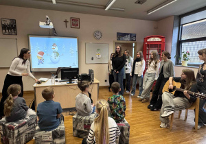 dzieci siedzą w półkolu i słuchają uczenic z liceum