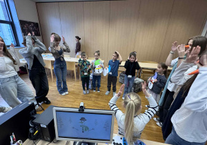 dzieci stoją w kole, pokazująć i śpiewając piosenke po angielsku z uczenicami liceum