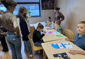 ziewci siedzą przy stoliku wykonując papierowe bałwanki, przy pomocy uczenic z liceum