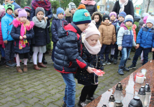 Dzieci składaja znicze pod pomnikiem 