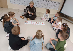 dzieci siedzą z panią na dywanie i uczą się nowych słów zwiazanych z pączkiem