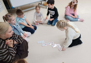 dzieci siedzą w kole i jedna dziewczynka układa domino