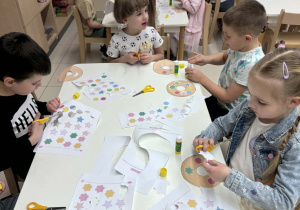 dzieci siedzą przy stoliku i wycinają swoje pączki